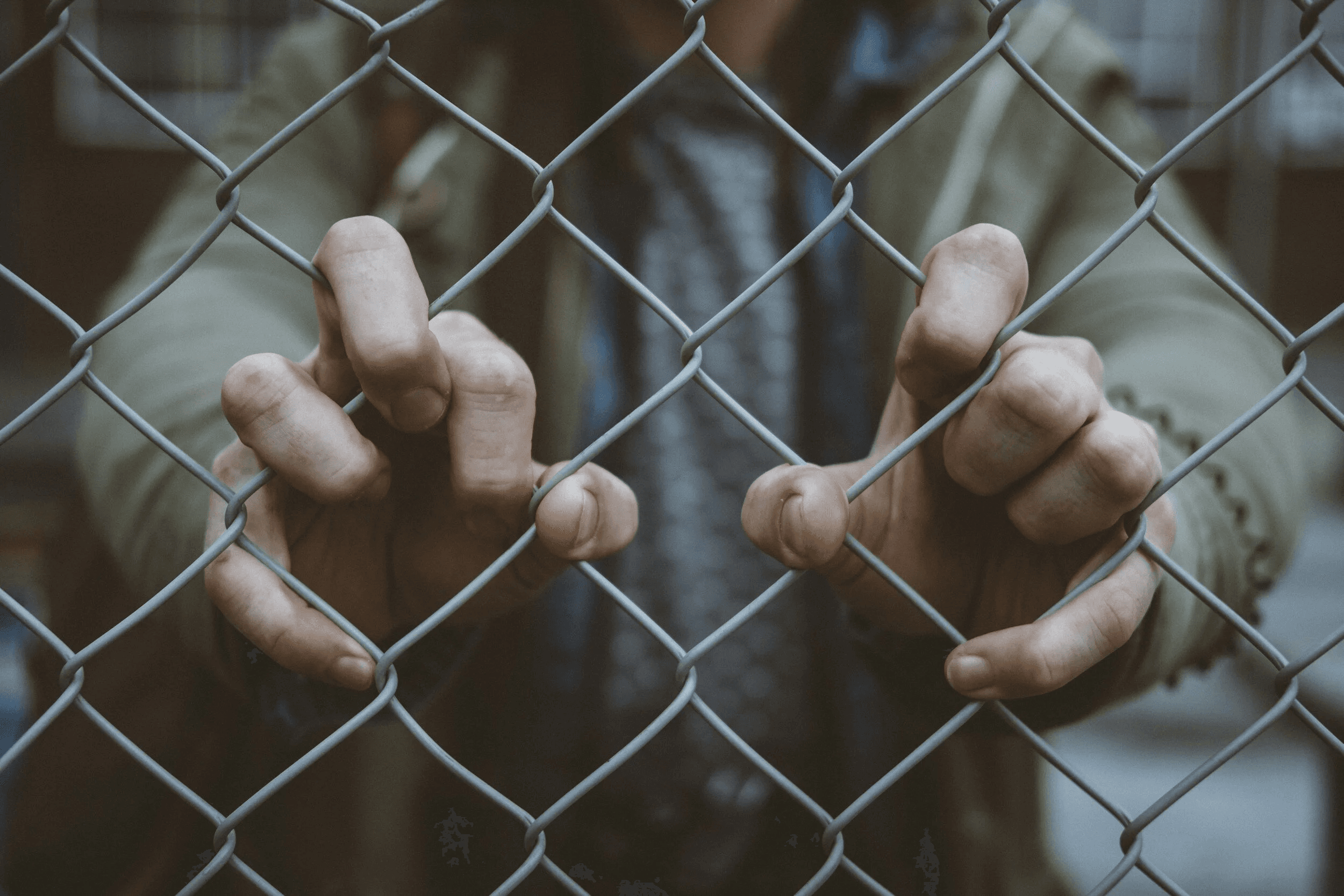 A person grips a chain-link fence with both hands