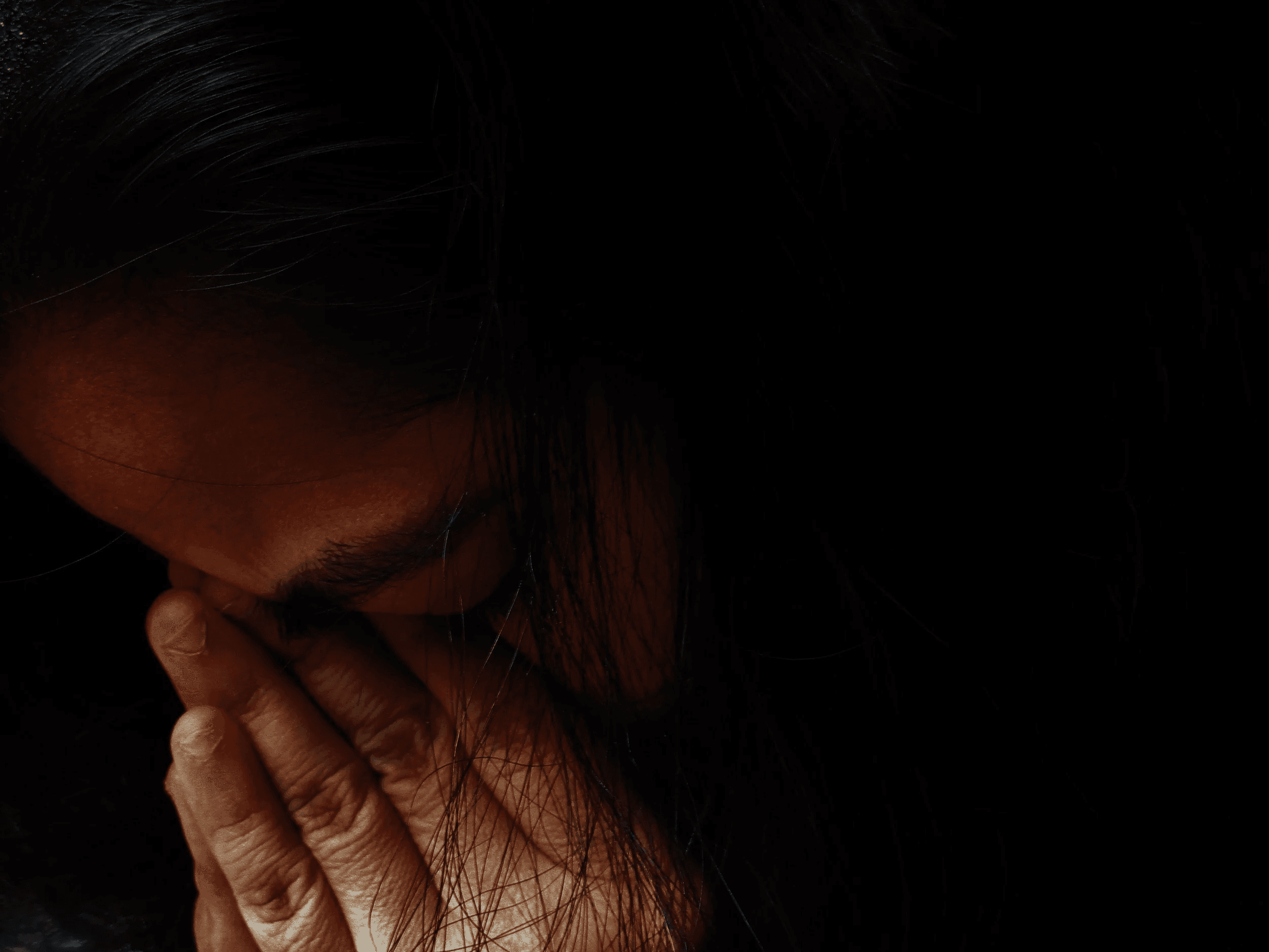 A woman in the dark bows her head and covers her face with her hand