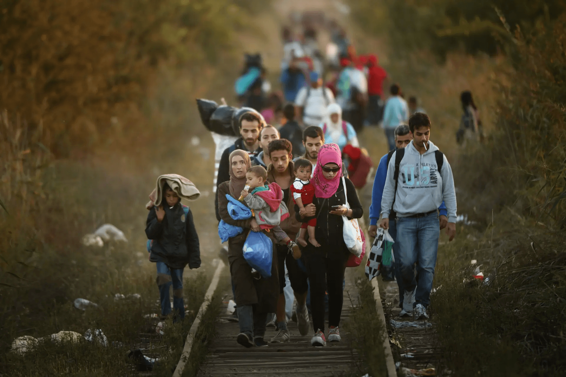 Geflüchtete Familien, einige mit Kindern und Taschen im Arm, gehen auf der Balkanroute entlang eines Bahngleises